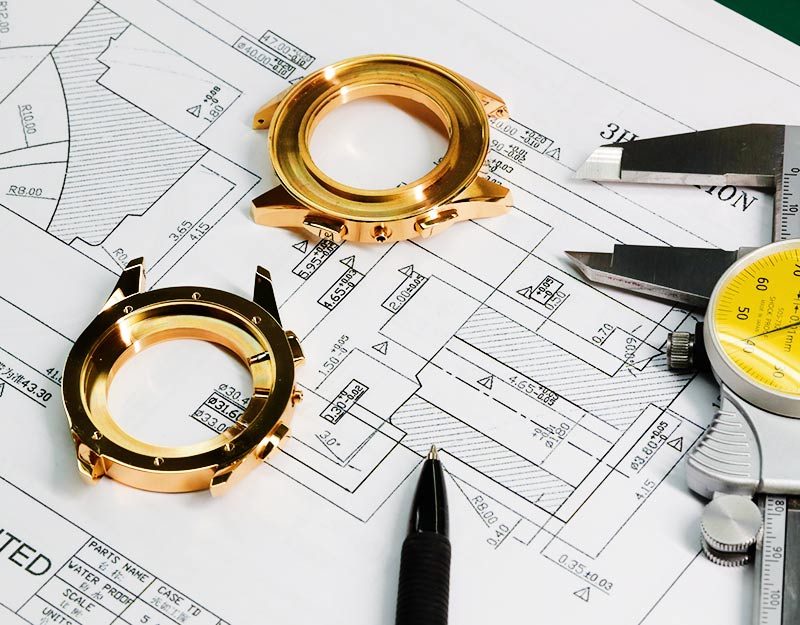 Gold cases laid on the technical drawings they were cut from.