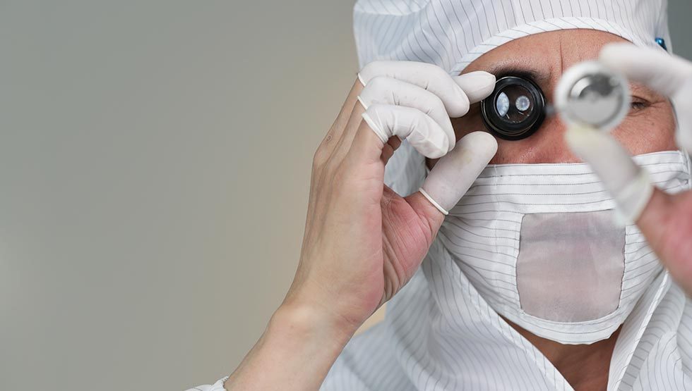Inspection through a loupe by an operator in cleanroom mask and cap.