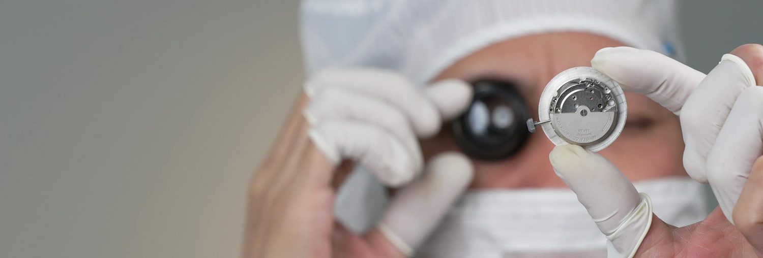 Gloved hands inspecting a watch through a loupe.